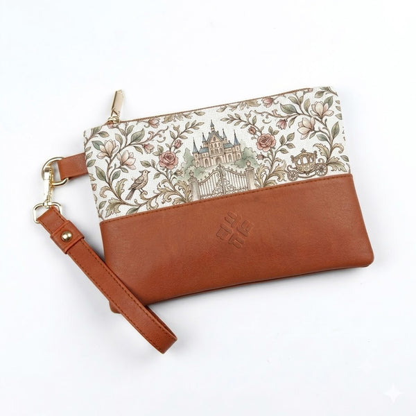 A rectangular wristlet featuring a fairytale castle, roses, and carriage illustration on canvas paired with a brown leather-like base and a detachable wrist strap.