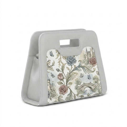 A modern, grey neoprene handbag with a cutout handle, featuring a detailed vintage print of castles, roses, and butterflies, positioned next to its white shoulder strap with black clasps against a white background.
