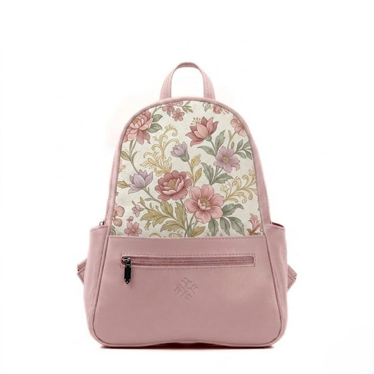 A structured mini backpack with a pink faux leather base and a top flap made of woven fabric printed with a vintage pattern of pink, mauve, and purple flowers with green leaves and gold filigree accents, featuring a front zipper and side pockets.